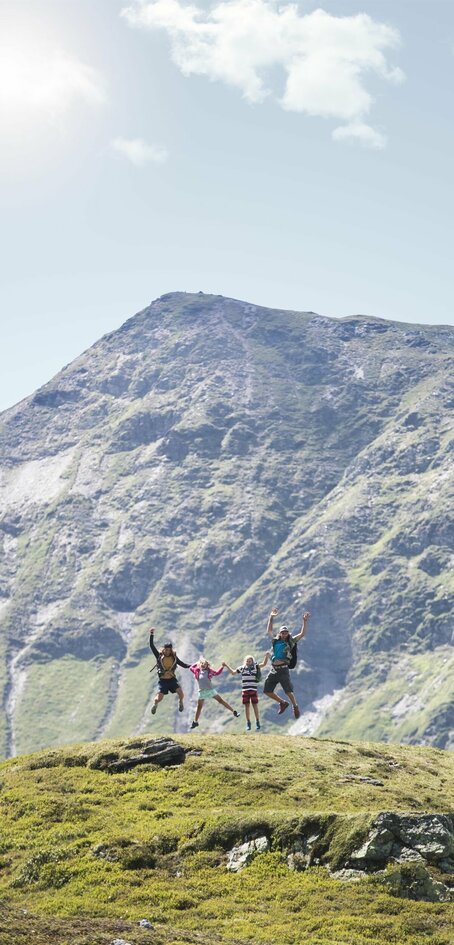 Familie macht einen Lufstsprung vor Gipfelpanorama