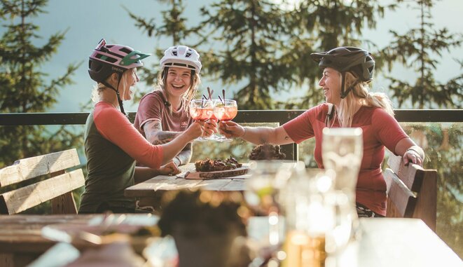 Drei Frauen in Mountainbikeausrüstung machen Rast auf der Alm