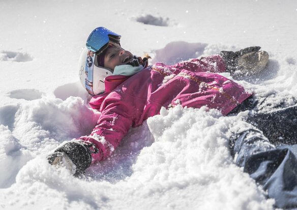 Kind mit Skiausrüstung liegt im Schnee